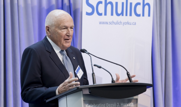 Robert Kremil, CM (MBA ’71, Hon LLD ’00) speaking at a podium with a Schulich banner in the background.