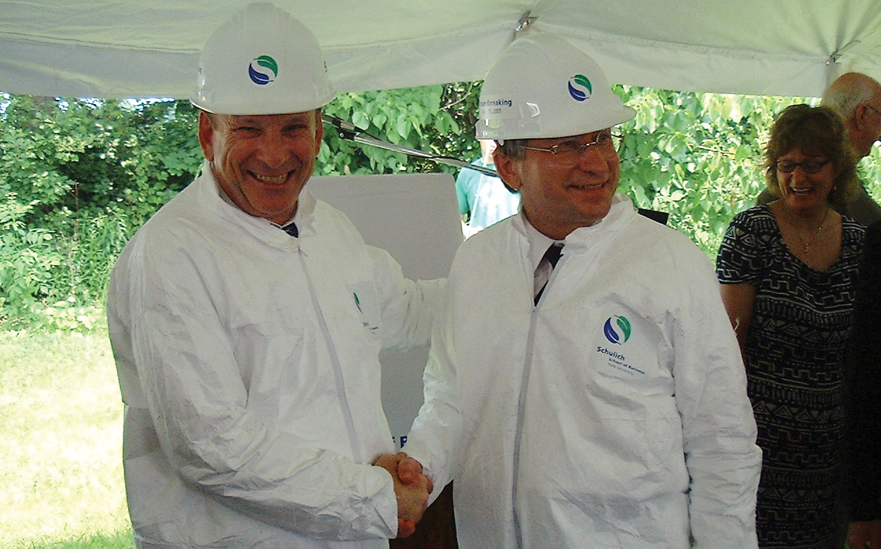 Seymour Schulich, OC (Hon LLD ’03) and Dean Emeritus Dezsö Horváth wearing hardhats and white jumpsuits, shaking hands at the ground-breaking ceremony for the Seymour Schulich Building.