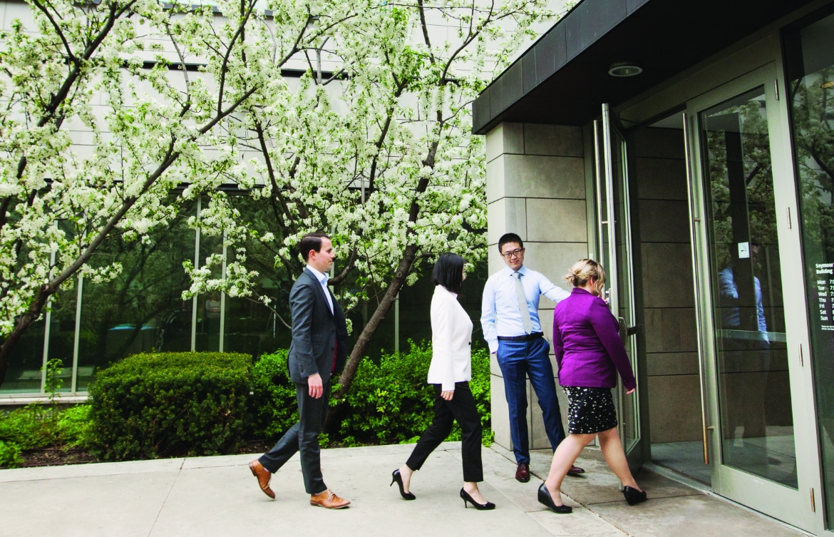 Four people walking through Schulich School of Business entrance with cherry blossom trees in the background.