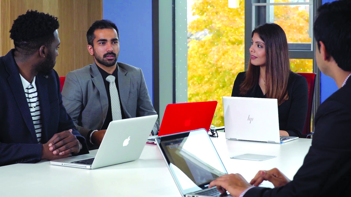 Four people with laptops in discussion during a boardroom meeting at the McEwen Building.