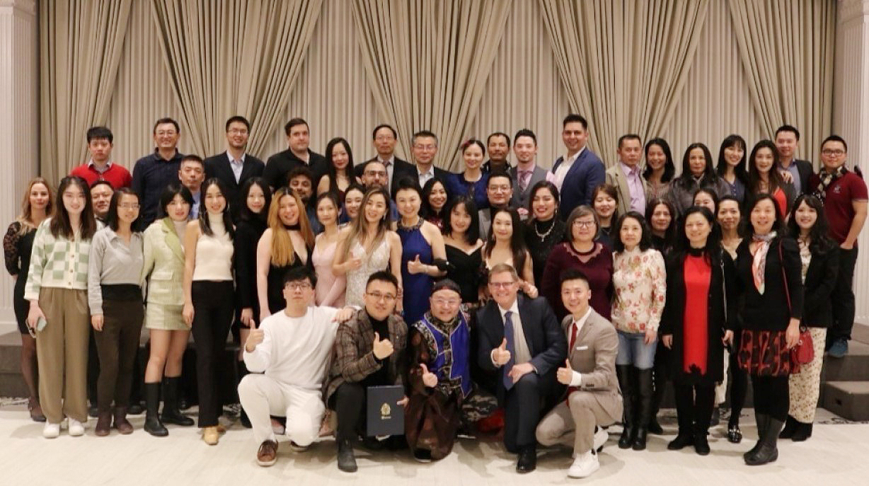 Three rows of Schulich alumni at a gala in front of an ornate curtain wall.